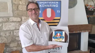 Ein Mann in einem weißen Hemd hält eine Kuchenbox mit einem Kuchen darin, der 50 Jahre Mitgliedschaft beim Sportverein Kühnring feiert.