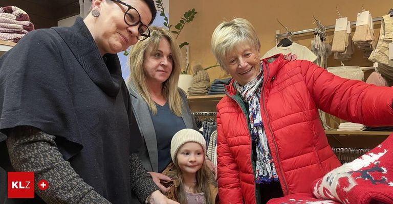 Drei Frauen und ein junges Mädchen stehen in einem Bekleidungsgeschäft. Die Frau links trägt eine Brille und einen grauen Mantel. Das Mädchen trägt eine Mütze.