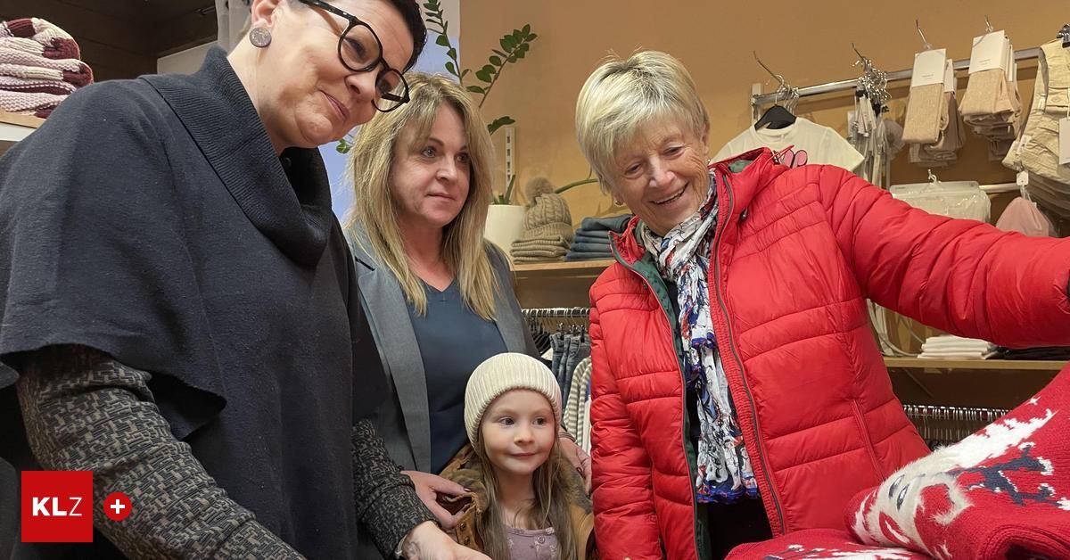 Drei Frauen und ein junges Mädchen stehen in einem Bekleidungsgeschäft. Die Frau links trägt eine Brille und einen grauen Mantel. Das Mädchen trägt eine Mütze.