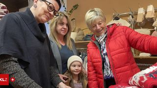 Drei Frauen und ein junges Mädchen stehen in einem Bekleidungsgeschäft. Die Frau links trägt eine Brille und einen grauen Mantel. Das Mädchen trägt eine Mütze.