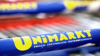 Eine Nahaufnahme eines blauen Einkaufswagengriffs mit der Aufschrift 'UNIMARK' und 'FRISCH FREUNDLICH OSTERREICH'.
