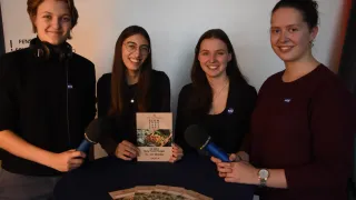 Vier Personen, zwei Männer und zwei Frauen, stehen um einen Tisch herum und halten Mikrofone. Sie lächeln und scheinen sich auf ein Interview vorzubereiten. Ein Büchlein mit dem Titel 'Slow Food Tage' liegt auf dem Tisch.