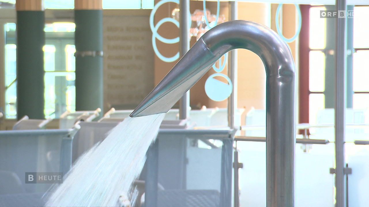 Ein Edelstahlhahn spritzt Wasser in einen Pool, mit einem dekorativen Design an der Wand dahinter.