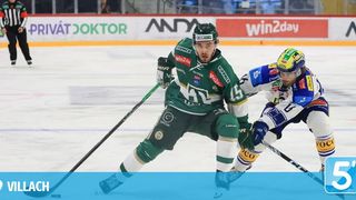 Zwei Eishockeyspieler treten auf dem Eis gegeneinander an, einer in Grün und der andere in Blau. Beide halten Schläger in der Hand, ein Spieler in einer defensiven Haltung. Die Eisbahn ist mit Sponsorenwerbung verziert.