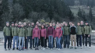 Eine Gruppe von Menschen, die Winterjacken tragen, steht in einer Reihe im Freien. Sie posieren wahrscheinlich für ein Gruppenfoto.