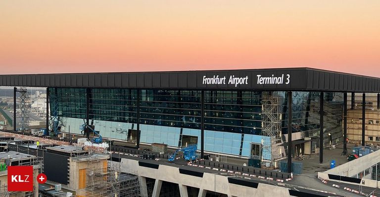 Eine Luftaufnahme des Terminals 3 des Flughafens Frankfurt während des Sonnenuntergangs. Das Terminal hat ein modernes Design mit großen Glasfenstern. Im Vordergrund sind Bauarbeiten zu sehen.