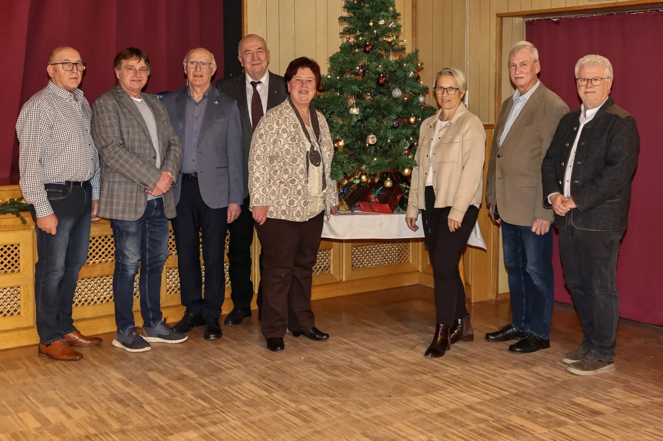 Eine Gruppe von sechs Personen steht in einem Raum, vielleicht für ein Gruppenfoto. Sie sind alle formell gekleidet. Hinter ihnen steht ein Weihnachtsbaum.