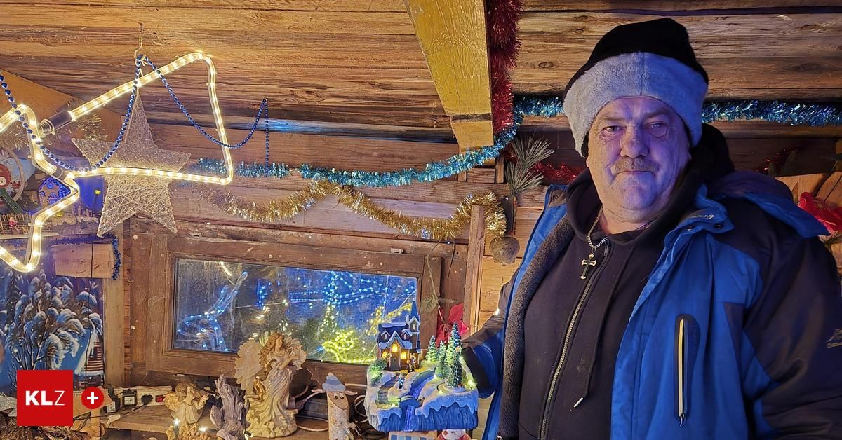 Ein Mann in einer Wintermütze und Jacke steht in einer Hütte mit Weihnachtsdekorationen und hält eine Winterszenen-Miniatur in der Hand.