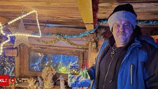 Ein Mann in einer Wintermütze und Jacke steht in einer Hütte mit Weihnachtsdekorationen und hält eine Winterszenen-Miniatur in der Hand.