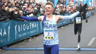 Ein Marathonläufer in einem blau-weißen Trikot mit der Nummer 7 feiert seinen Sieg, während er mitten im Rennen läuft.