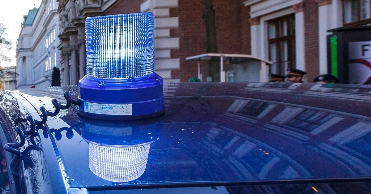 Ein blauer Notblitzer befindet sich auf einem Auto. Das Auto steht vor einem Gebäude mit Ziegelsteinwänden.