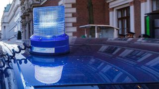 Ein blauer Notblitzer befindet sich auf einem Auto. Das Auto steht vor einem Gebäude mit Ziegelsteinwänden.