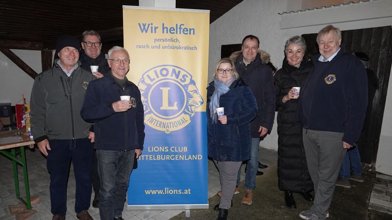 Fünf Menschen stehen vor einem Lions Club-Banner und lächeln. Sie halten alle Tassen. Der Schriftzug auf dem Banner lautet 'Wir helfen persönlich, rasch und unbürokratisch'.