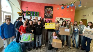 Eine Gruppe von Schülern hält ein Schild mit einem großen Spendenbetrag und Kisten in einem farbenfrohen Raum.