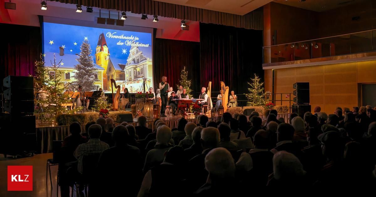 Ein Weihnachtskonzert findet in einer Halle statt. Eine Gruppe von Menschen tritt auf der Bühne mit Weihnachtsdekorationen und einer großen Leinwand hinter ihnen auf. Das Publikum sitzt vor der Bühne.