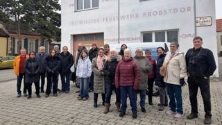 Eine Gruppe von Menschen steht vor einem Gebäude mit der Aufschrift 'Freiwillige Feuerwehr Probst'. Sie tragen Winterkleidung. Ein weißer Van ist vor dem Gebäude geparkt.