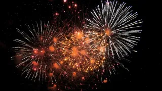 Ein nächtliches Feuerwerk mit roten, weißen und gelben Explosionen, die den dunklen Himmel erhellen und ein atemberaubendes und farbenfrohes Spektakel bieten.