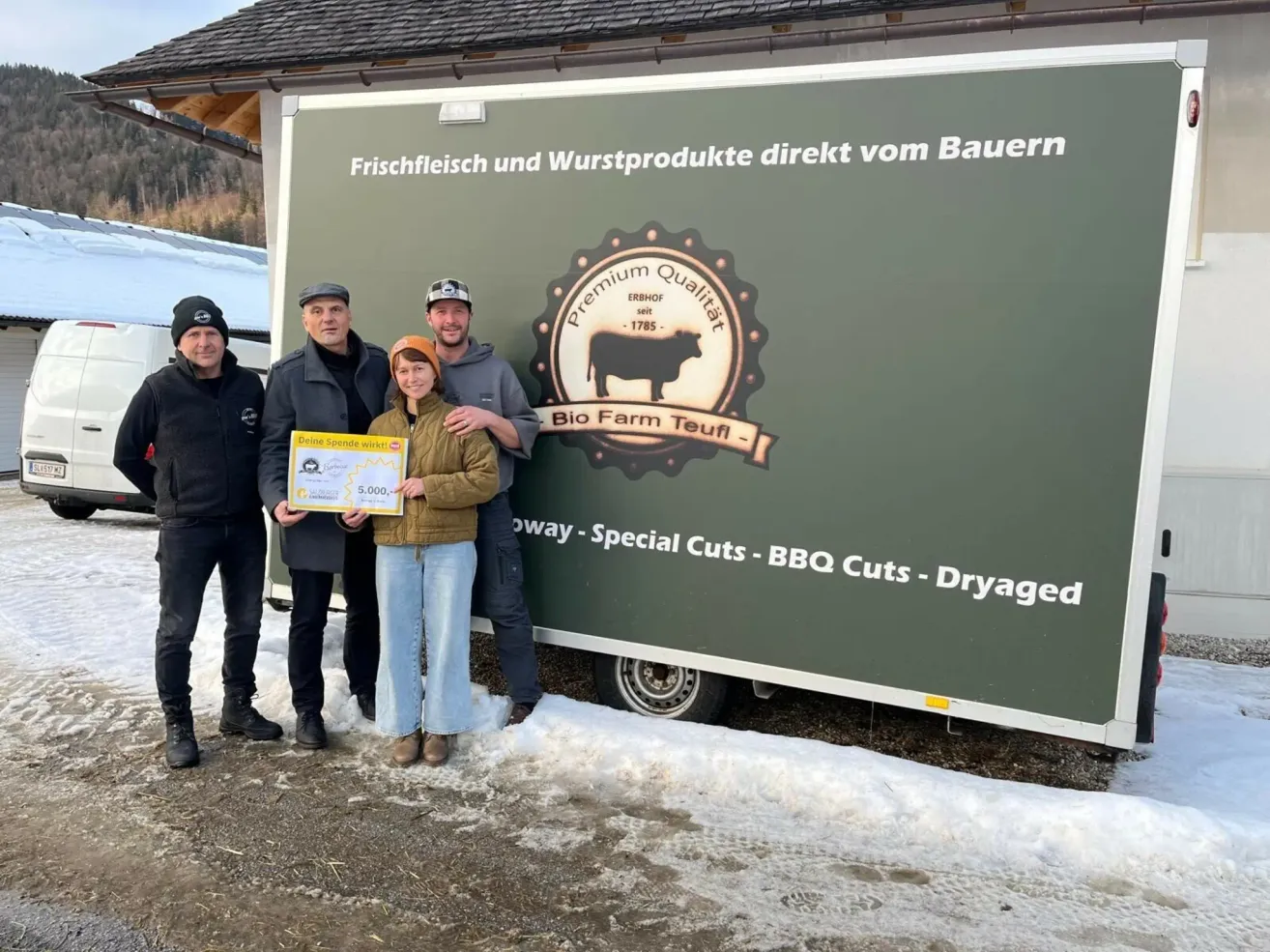 Fünf Personen stehen vor einem Lastwagen. Eine Frau hält eine Urkunde. Der Lastwagen hat einen grünen Hintergrund und weiße Text, der 'Premium Qualität Bio Farm Teufel - Special Cuts - BBQ Cuts - Dryaged' lautet.