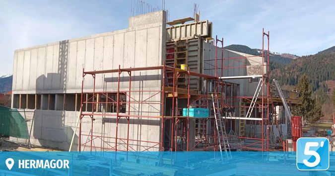 Ein Betongebäude im Bau mit roten Gerüsten. Im Hintergrund sind Berge sichtbar, und der Standort befindet sich in der Nähe eines Ortes namens Hermagor.