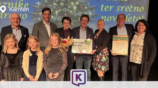 Eine Gruppe von Erwachsenen und Kindern steht lächelnd für ein Foto vor einer Weihnachtsbaum- und Hintergrundkulisse zusammen. Sie halten Zertifikate in den Händen.