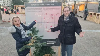 Ein Mann und eine Frau stehen vor einem Schild und diskutieren über die Zukunft von Superhelden. Das Schild enthält ein Flussdiagramm mit Symbolen und Text.