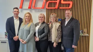 Fünf Personen, drei Frauen und zwei Männer, stehen lächelnd für ein Foto vor einem FIDLAS-Schild.