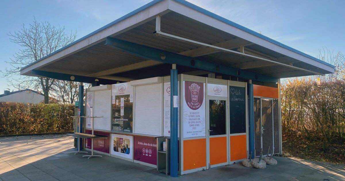 Ein Imbiss mit einer Speisekarte steht unter einem Metalldach. Der Kiosk ist orange und weiß gestrichen, und draußen stehen Tische und Stühle.