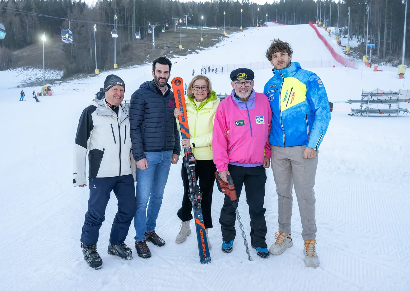 Fünf Personen stehen im Schnee mit Skiausrüstung. Ein Skilift ist im Hintergrund.