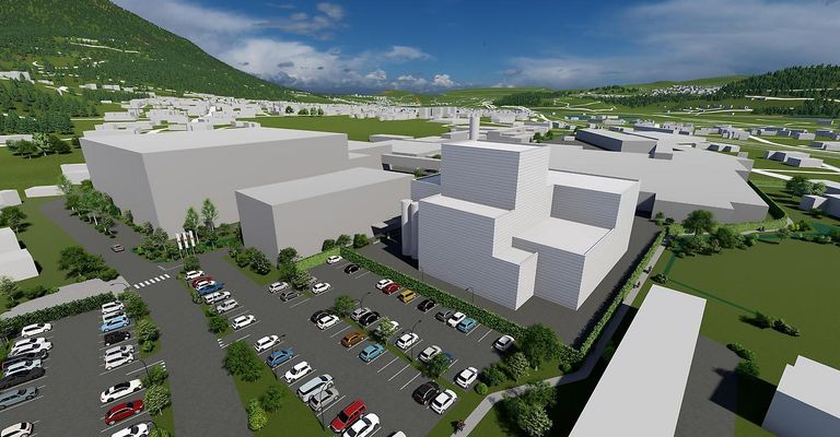 Eine Vogelperspektive einer modernen Industrieanlage mit einem großen Parkplatz, umgeben von Grünflächen und einem Berg im Hintergrund.