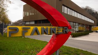 Ein rotes Schild mit dem Wort Pfannier in grauen Buchstaben steht vor einem Gebäude mit vielen Fenstern.