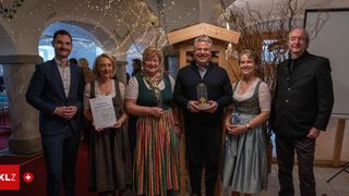 Eine Gruppe von Menschen steht in einem Raum, lächelt, einer Mann hält eine Trophäe und eine andere eine Urkunde.