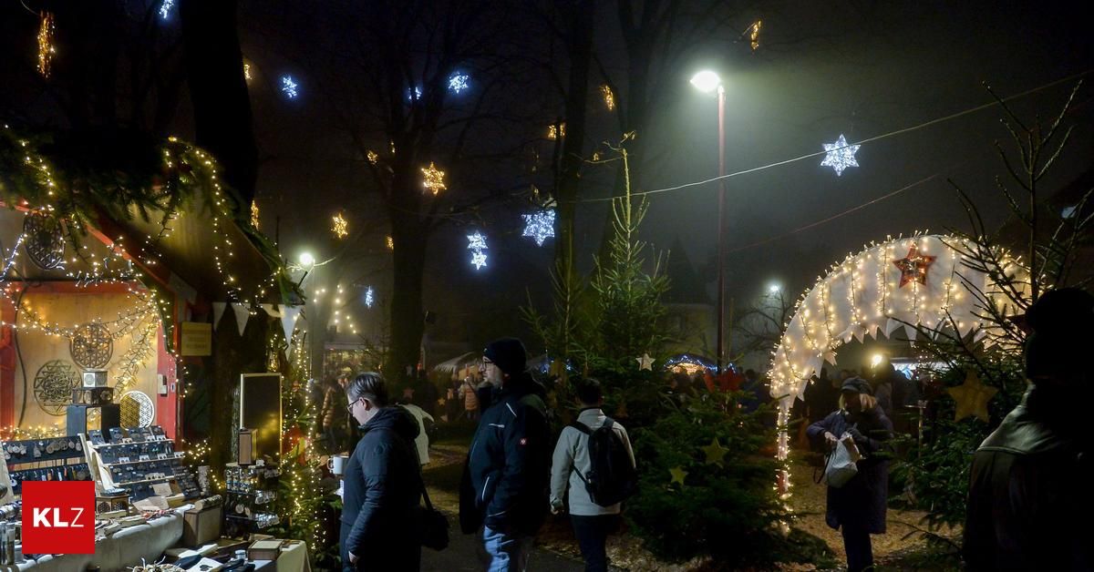 Menschen gehen auf einem festlich geschmückten Außenmarkt, mit Bäumen, die mit Ornamenten und Lichtern geschmückt sind. Ein Mann mit Rucksack und eine Frau mit Plastiktüte gehören zur Menge.