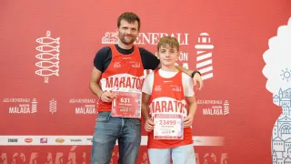 Zwei Männer stehen vor einem roten Hintergrund, einer trägt ein rotes Shirt mit MARATHON, das Nummer 631 hält. Der andere trägt ein rotes Shirt mit MARATHON und der Nummer 23499, eine Medaille haltend.