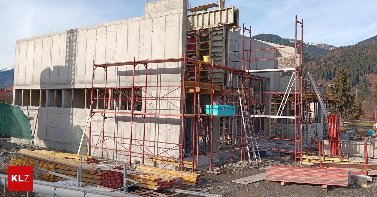 Eine Baustelle mit einer Betonwand und Gerüsten, einem gelben Eimer auf dem Gerüst und einer blauen Kiste auf dem Boden.