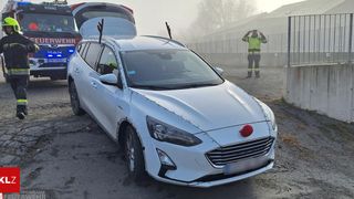 Ein weißer SUV mit Weihnachtsdekoration, einschließlich roter Geweihe und einer roten Nase, ist draußen geparkt. Ein Mann in einer reflektierenden Weste steht in der Nähe.