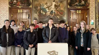 Eine Gruppe von Schülern und Erwachsenen steht in einem eleganten Raum und lächelt für ein Foto. Ein großes Gemälde ist an der Wand hinter ihnen.