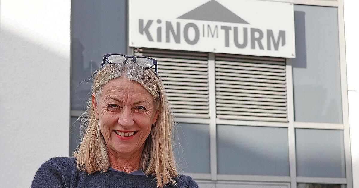 Eine ältere Frau mit blondem Haar lächelt in die Kamera und steht vor einem Gebäude mit dem Schild 'KiNO IM TURM'.