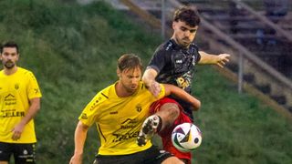 Zwei Fußballspieler sind in einer dynamischen Pose. Ein Spieler in Gelb versucht, den Ball zu schießen, während der andere in Schwarz versucht, zu blocken.