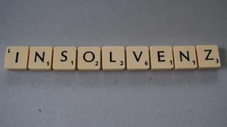 Eine Reihe von Scrabble-Steinen, die das Wort 'LÖSEN' auf einem grauen Hintergrund bilden. Jeder Buchstabenstein hat eine Nummer darunter.