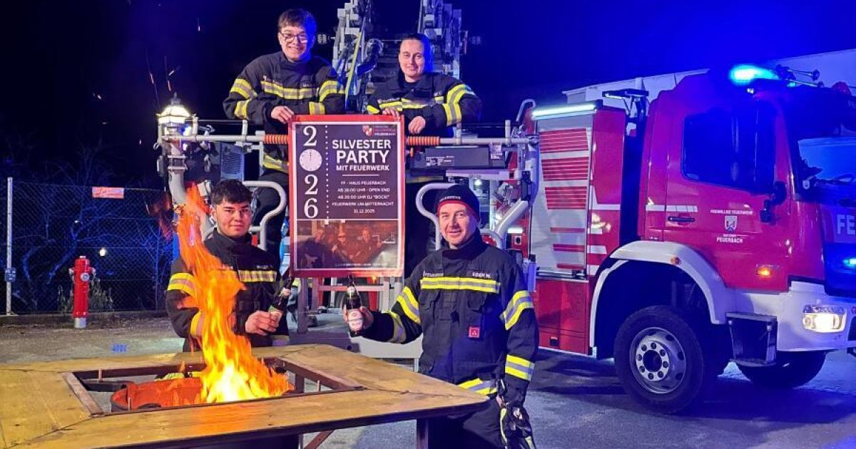 Vier Feuerwehrleute stehen neben einem Feuerwehrauto, zwei halten Flaschen und einer hat ein Schild mit der Aufschrift Silvester Party mit Feuerwehr.