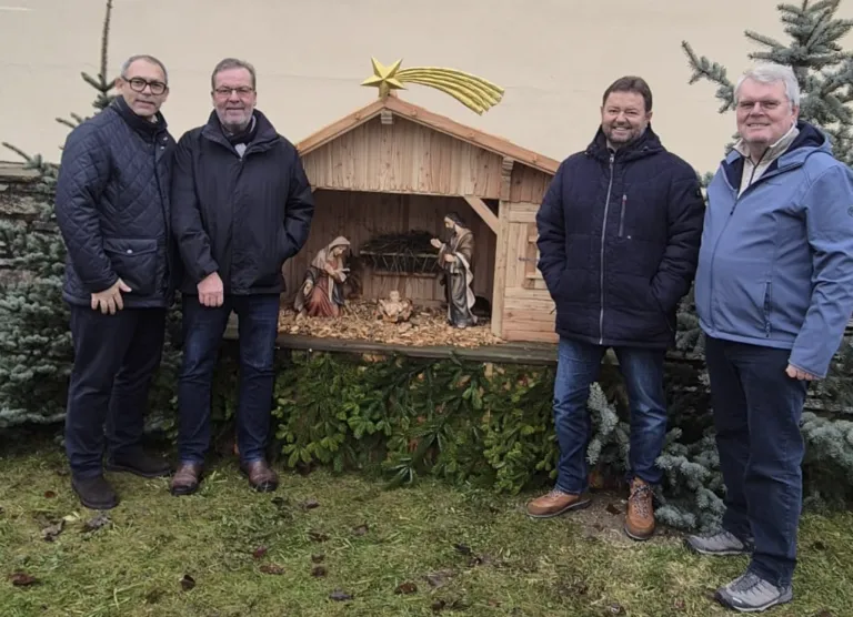 Vier Männer stehen vor einer Krippe mit Baby Jesus, Maria und Josef, alle in Winterkleidung.