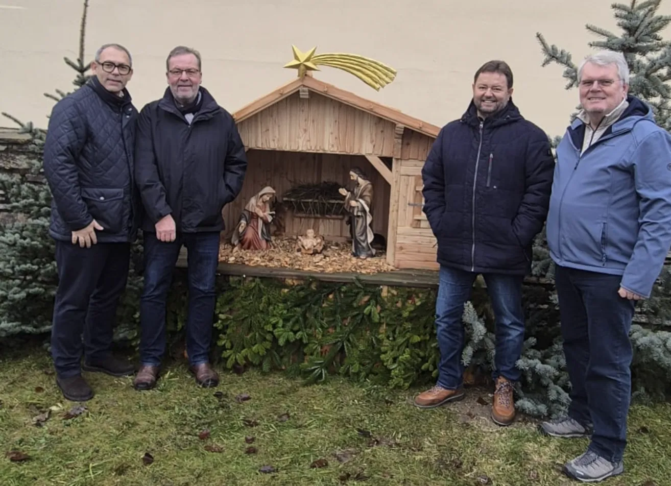 Vier Männer stehen vor einer Krippe mit Baby Jesus, Maria und Josef, alle in Winterkleidung.