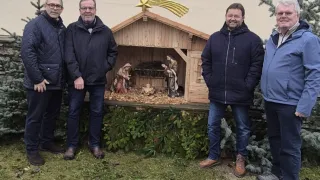 Vier Männer stehen vor einer Krippe mit Baby Jesus, Maria und Josef, alle in Winterkleidung.