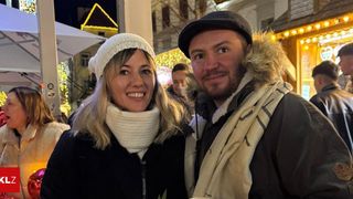 Ein lächelndes Paar bei einer festlichen Veranstaltung im Freien, mit winterlichem Hintergrund und Lichtern.