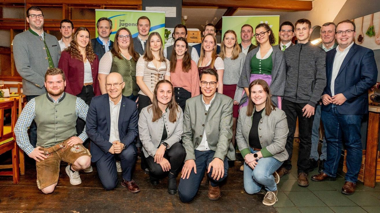 Eine Gruppe von Menschen, darunter sowohl Männer als auch Frauen, posiert für ein Foto in einem Raum mit Holzboden und grünen Bannern. Einige tragen Brillen und Sneakers.