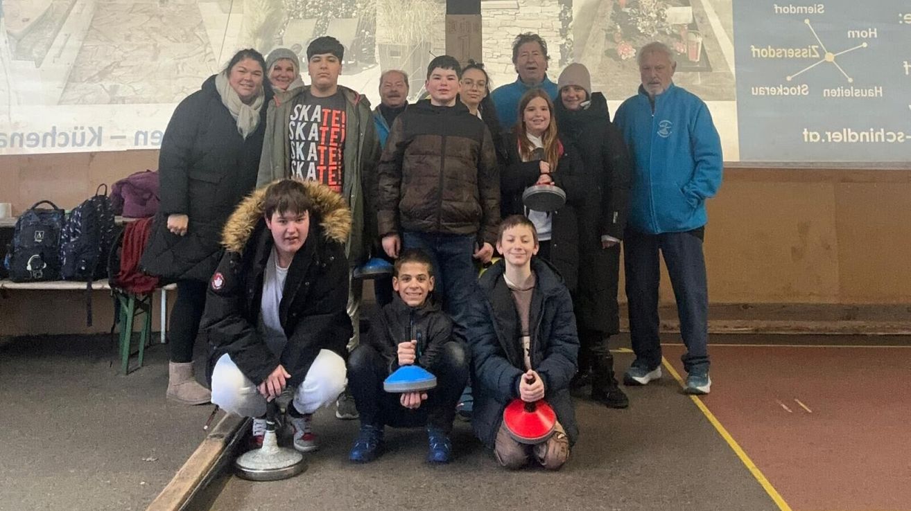 Eine Gruppe von Menschen, darunter mehrere Kinder, posiert für ein Foto. Sie halten verschiedene Gegenstände in der Hand und stehen vor einer Kulisse.