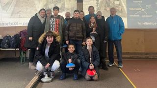 Eine Gruppe von Menschen, darunter mehrere Kinder, posiert für ein Foto. Sie halten verschiedene Gegenstände in der Hand und stehen vor einer Kulisse.