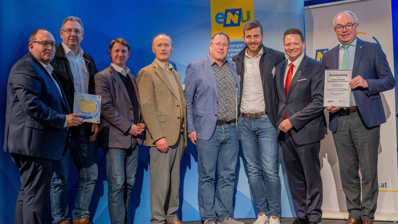 Fünf Männer stehen zusammen vor einer blauen Wand mit dem Logo und Namen 'eNU'. Sie sind alle in formeller Kleidung gekleidet.