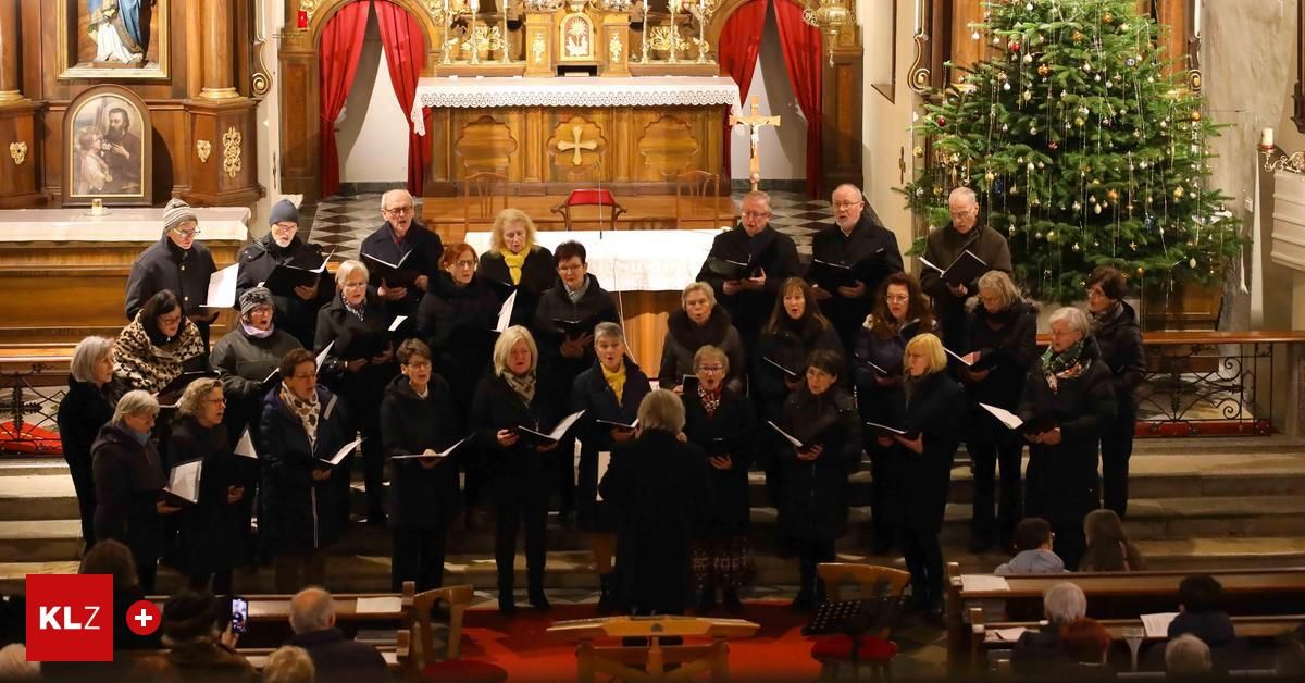 Ein Chor älterer Menschen, gekleidet in Schwarz und Weiß, singt in einer Kirche, mit einem Altar hinter ihnen. Der Altar ist mit einem goldenen Kreuz und Kerzen geschmückt. Ein Weihnachtsbaum steht auf der rechten Seite.