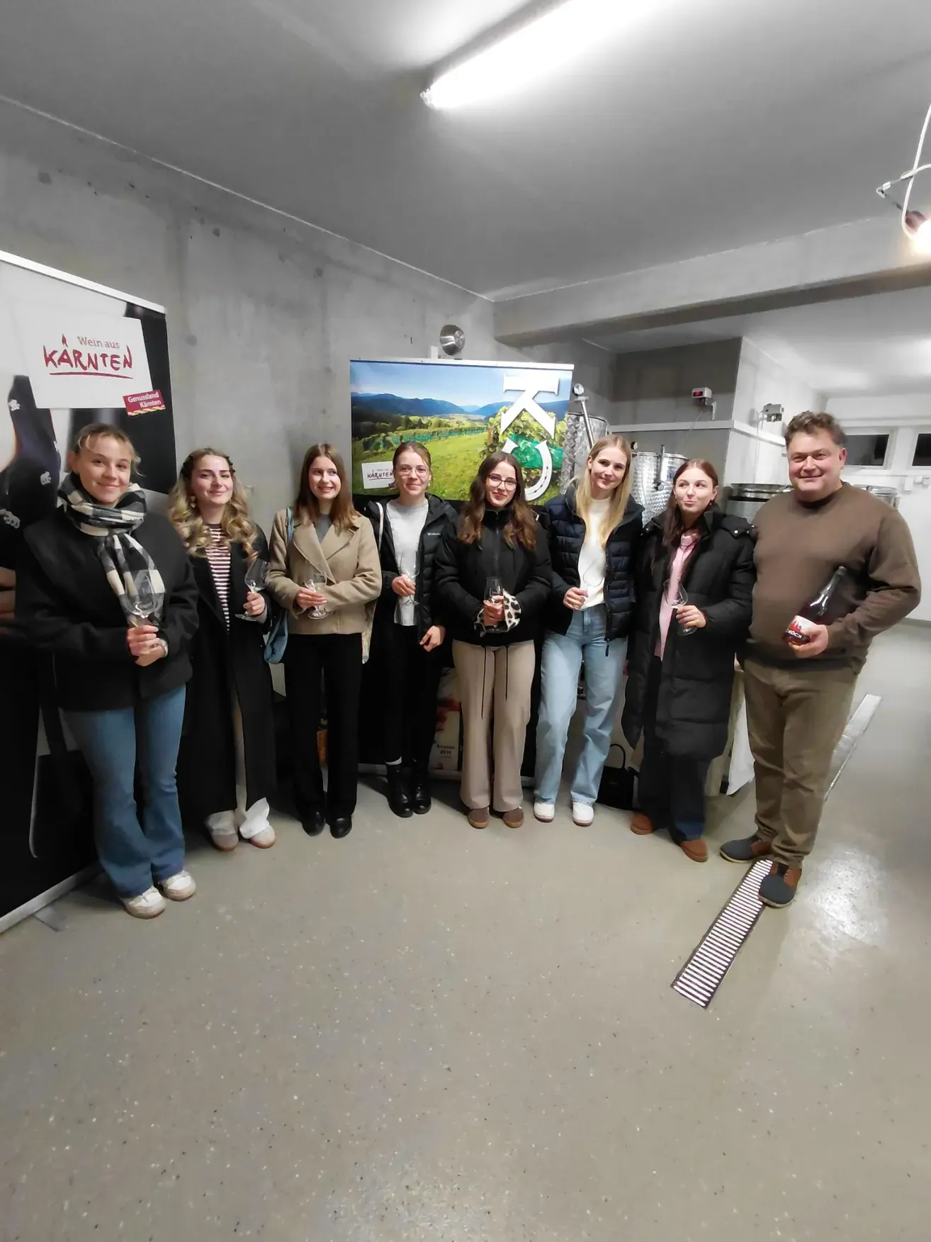 Eine Gruppe von Menschen, darunter Frauen mit Weinglas, posiert für ein Foto in einem Raum mit einem Banner.